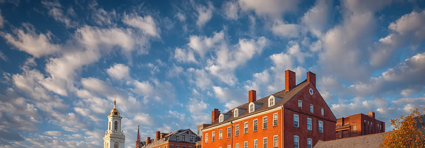 Historic Boston waterfront — red brick colonial buildings with church steeple reflected in perfectly still harbor water, dramatic cloud sky