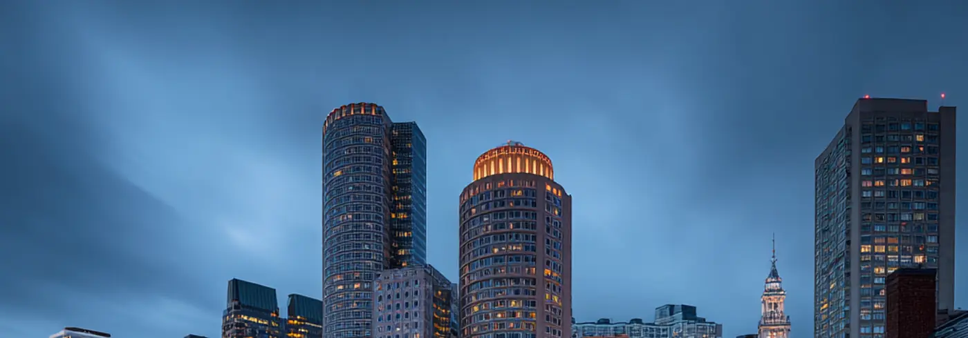 Boston Fan Pier area at blue hour — canal with docked boats, cobblestone street with car light trails, historic and modern architecture
